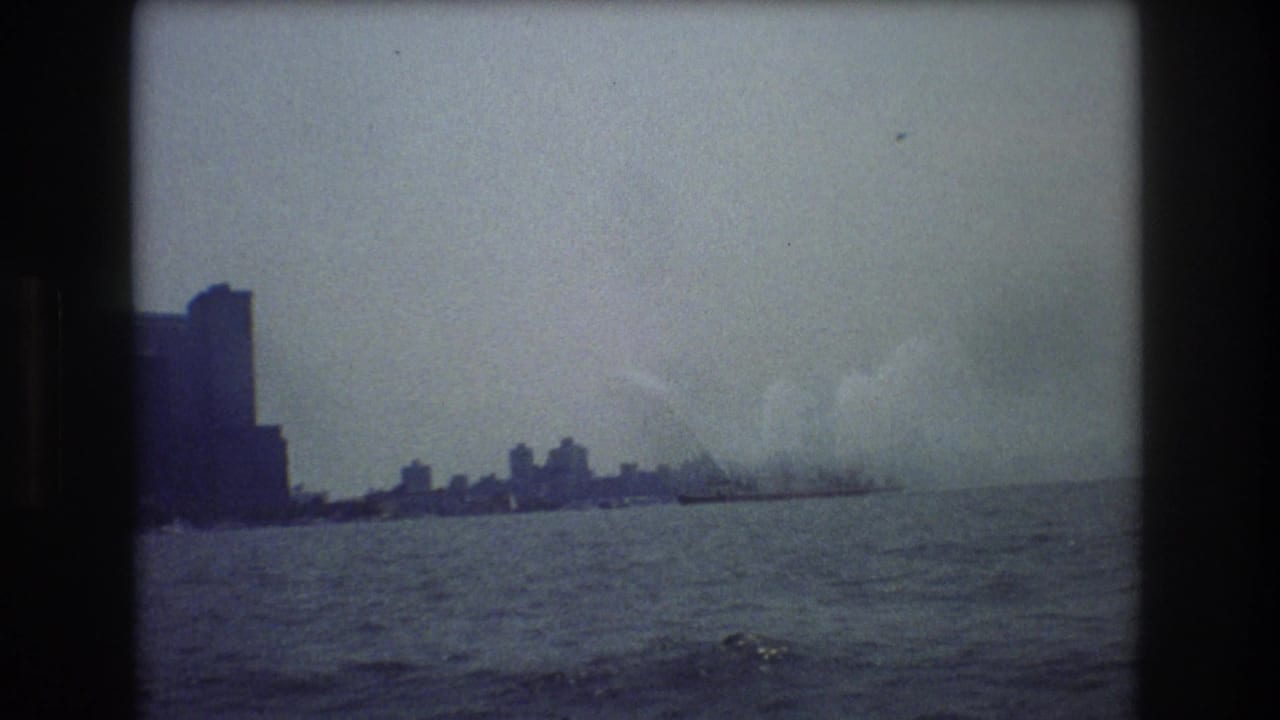 Distant city skyline across water with smoke or steam at right.