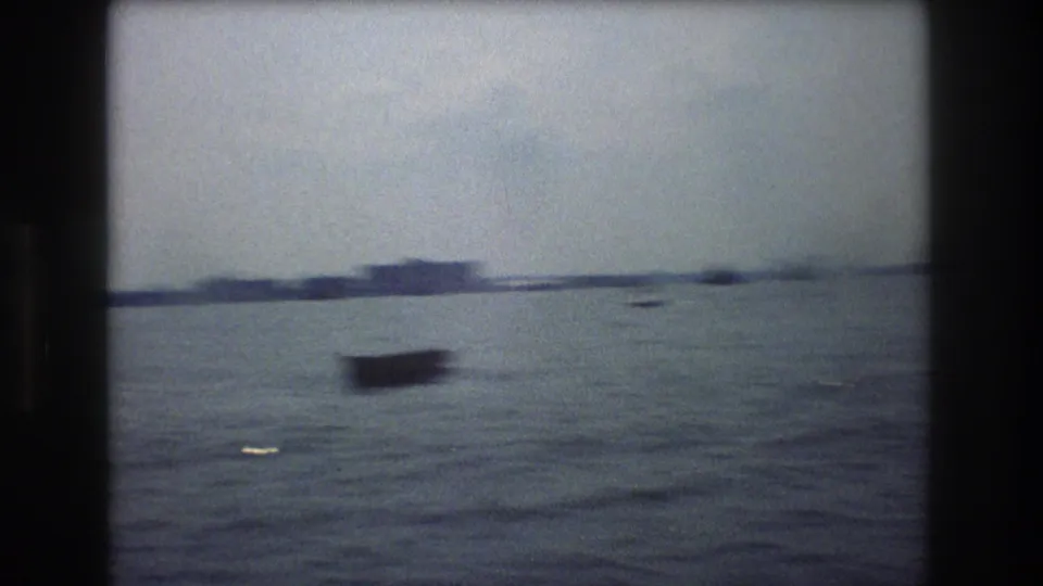 Small craft on New York City harbor water in 1976, with low shoreline and haze visible across the background.