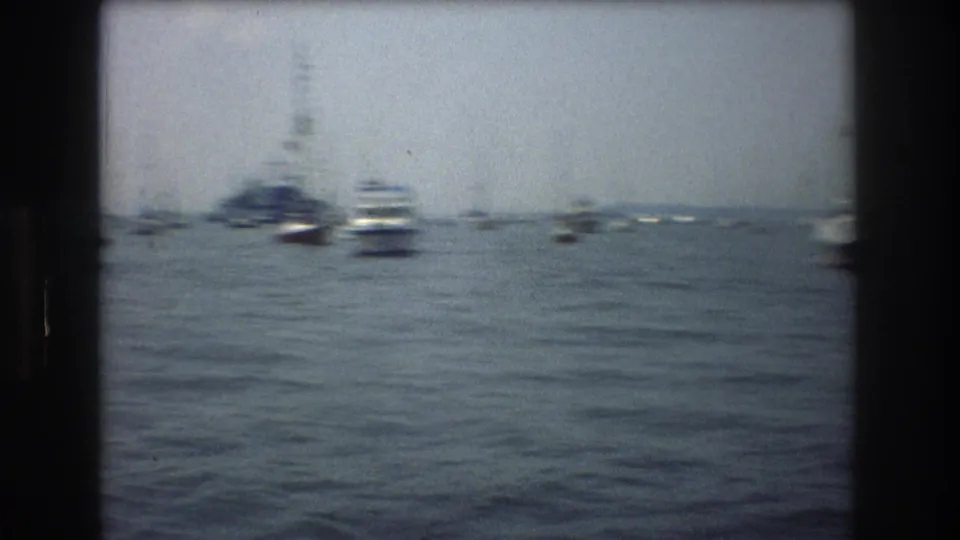 Several small boats on New York City harbor water in 1976, filmed from a moving offshore boat with soft grain and haze.