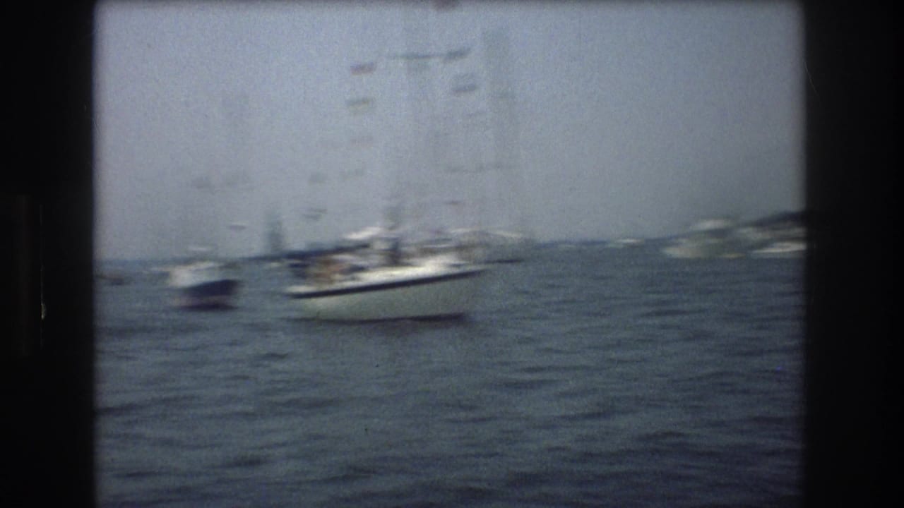 1976 New York City 8mm frame showing sailboats and small boats spread across choppy marina water beneath a hazy cloudy sky.