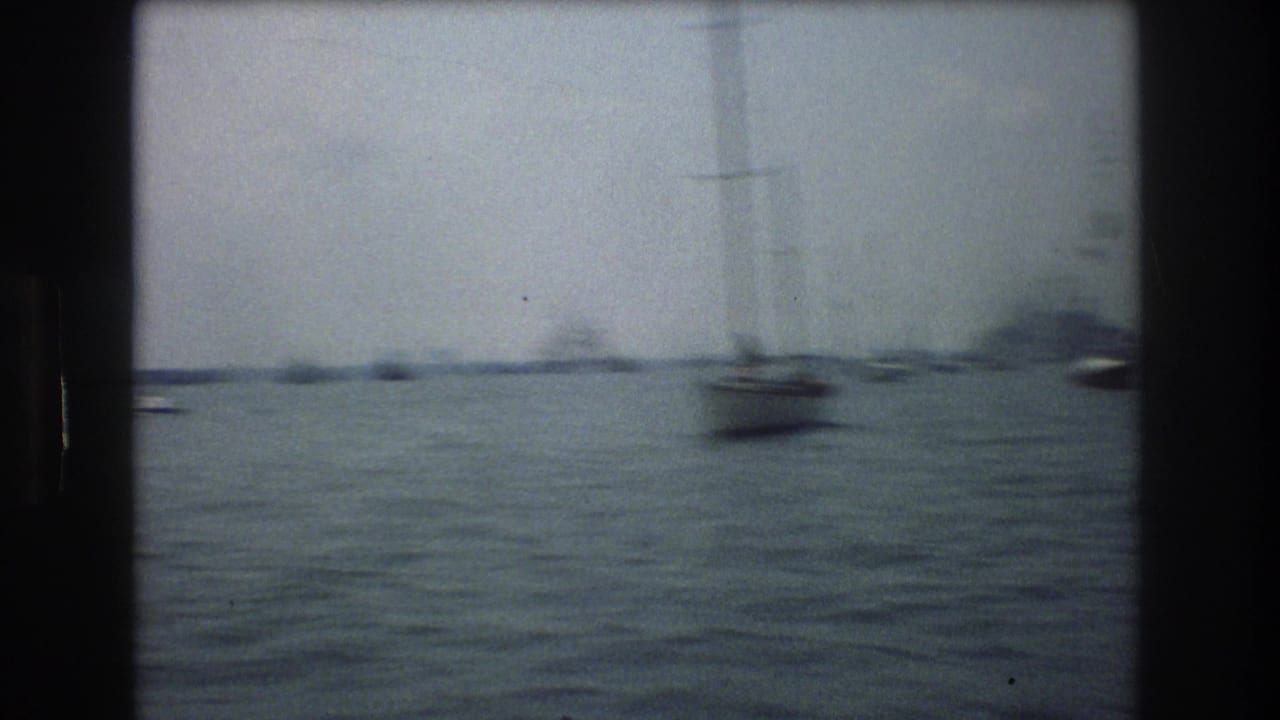 1976 New York City 8mm frame showing choppy harbor water, distant small boats, sailboat masts, and dark film gate edges.