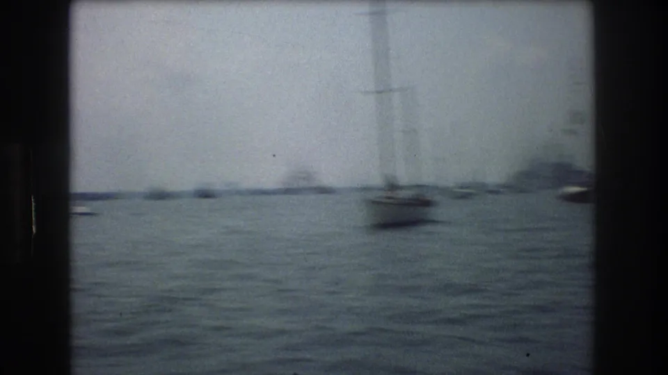 1976 New York City 8mm frame showing choppy harbor water, distant small boats, sailboat masts, and dark film gate edges.