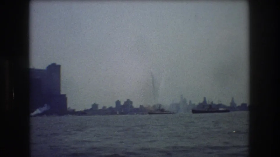 1976 New York City harbor frame with sailboats, a low distant skyline, choppy water, haze, and strong dark 8mm frame borders.