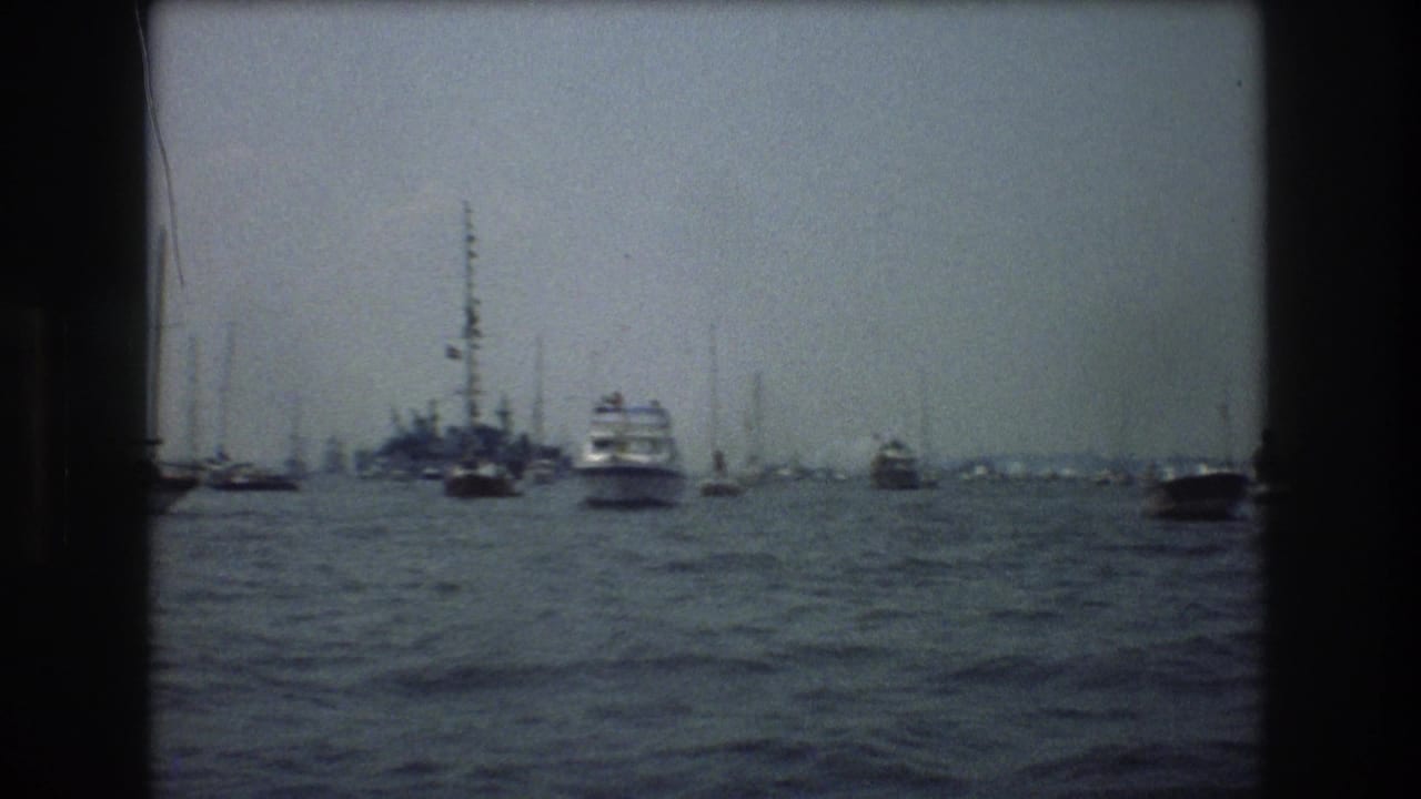 Multiple boats on harbor water with a distant skyline and tall masts.