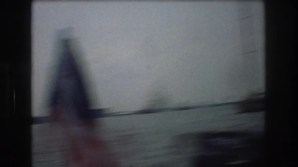 Motion-blurred 8mm harbor frame from New York City in 1976, with a sailboat passing close to the camera and water stretching behind it.