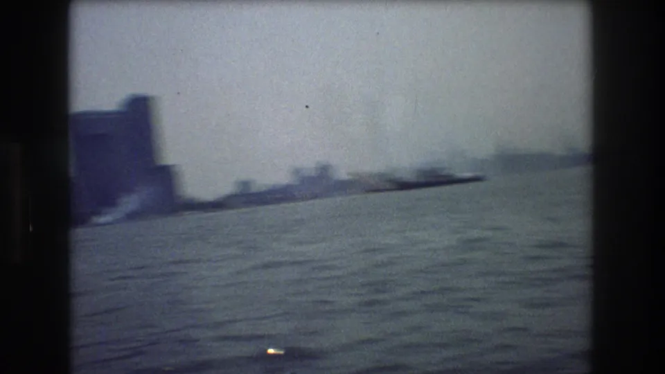 Hazy 1976 New York City harbor frame with choppy water, small distant vessels, and a soft skyline shape along the horizon.