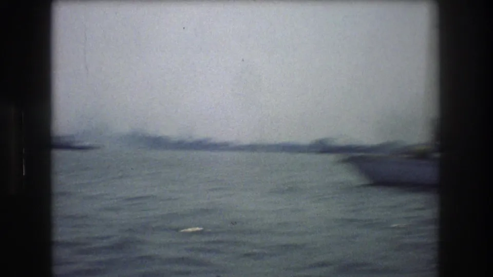 Soft, motion-blurred 8mm frame from a boat on New York Harbor, with water filling most of the view and a vessel shape near the right edge.