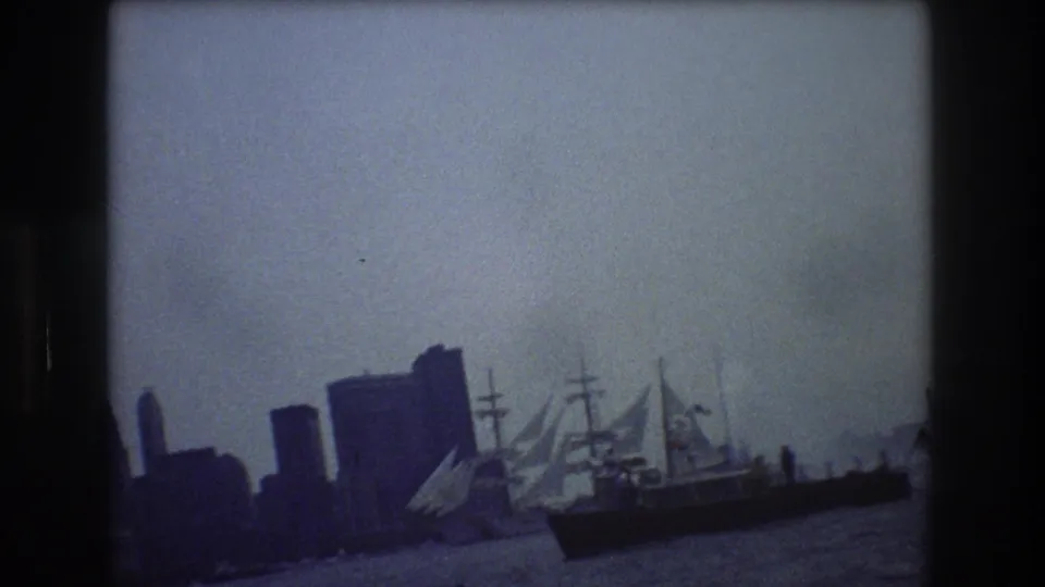 1976 8mm frame showing a tall-masted ship on New York Harbor with the city skyline hazy in the background.