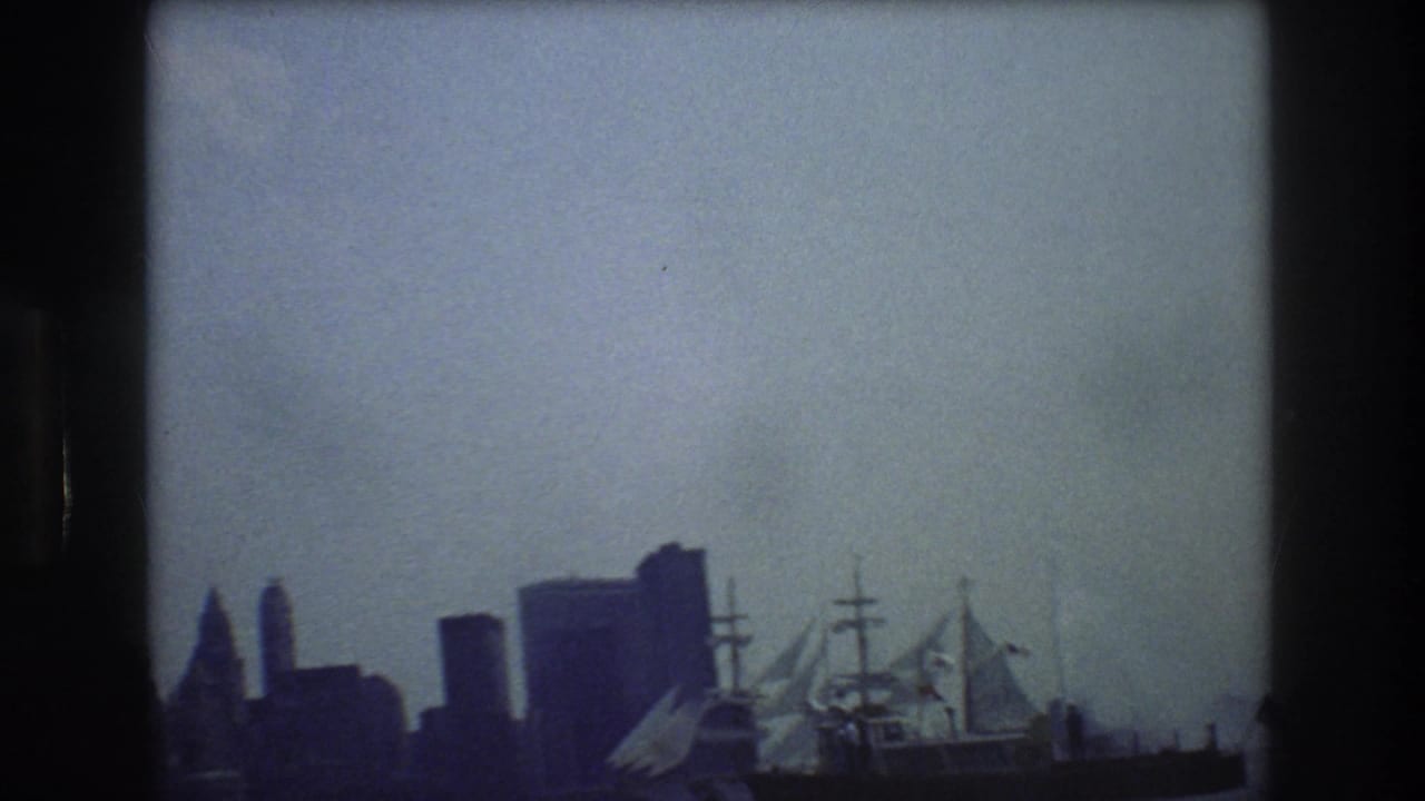 Sailing ship and New York City skyline seen across harbor water.