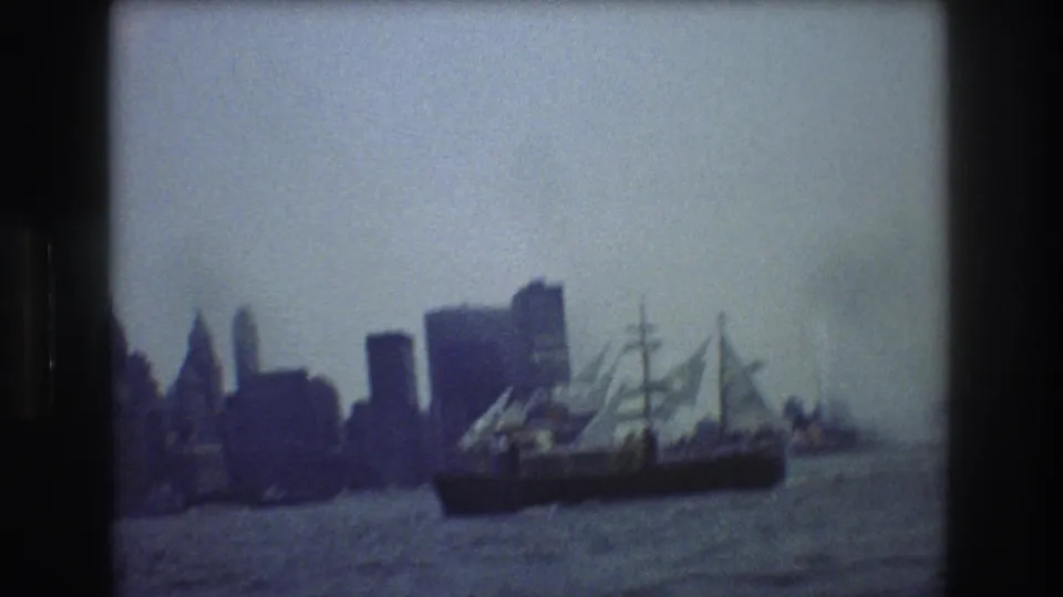 The sailing ship appears lower in the frame as the handheld 8mm camera records harbor water, skyline silhouettes, and pale sails.