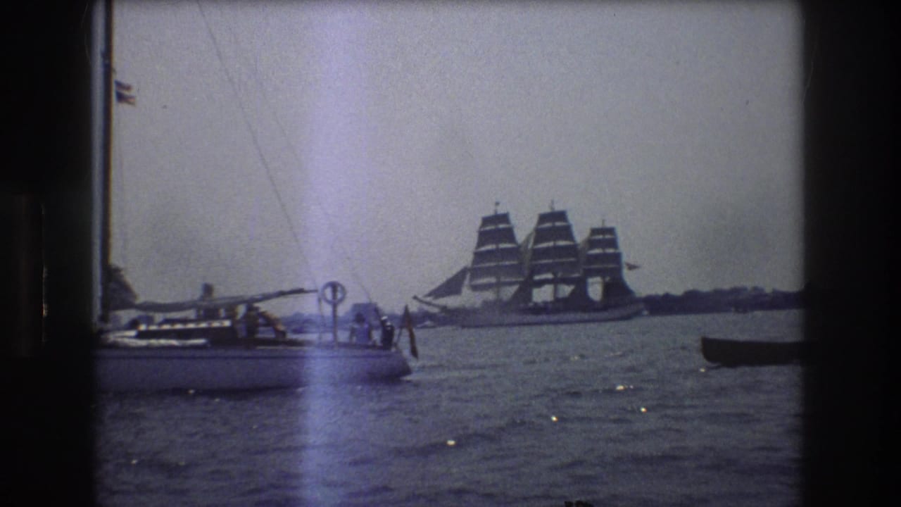 1976 New York City 8mm frame showing a small sailboat with people aboard and a distant three-masted sailing ship under sail across the water.