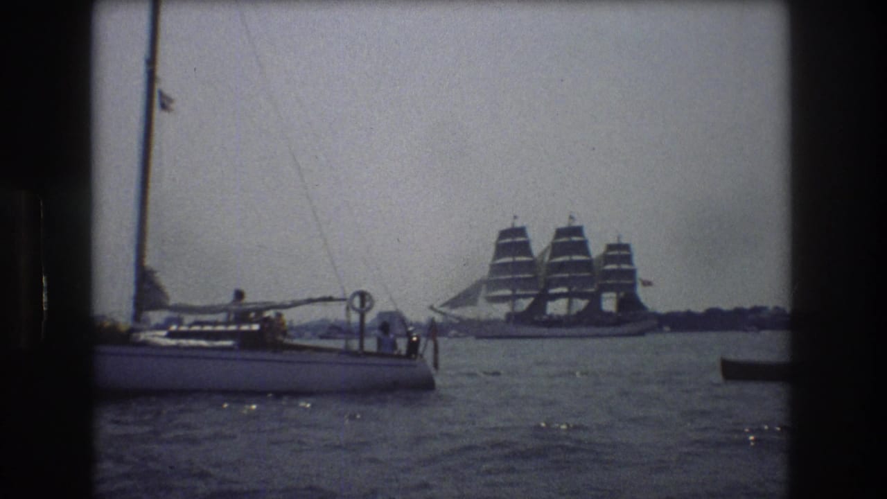 A sailboat crosses the foreground as a large three-masted ship moves behind it.