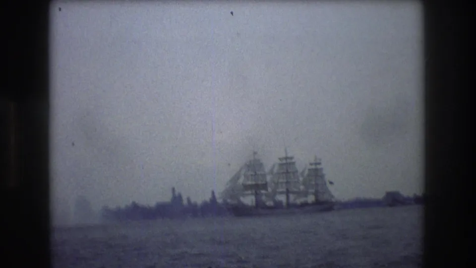 1976 New York City 8mm frame showing a three-masted sailing ship near a hazy shoreline or skyline, with open water in the foreground.