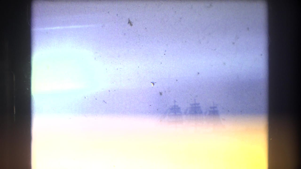 1976 New York City home-movie frame with heavy light exposure and a faint multi-masted ship visible near the harbor horizon.