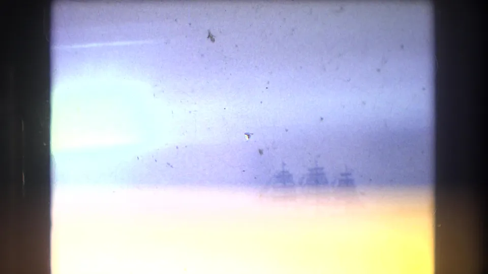 1976 New York City home-movie frame with heavy light exposure and a faint multi-masted ship visible near the harbor horizon.