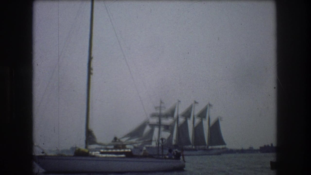 1976 New York City-area harbor footage showing a foreground sailboat with a tall mast and a larger multi-masted sailing vessel under sail in the background.