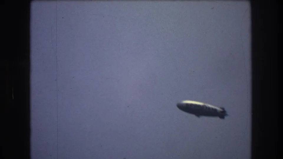 Distant blimp-like airship near the right side of the frame against a muted blue-gray sky.