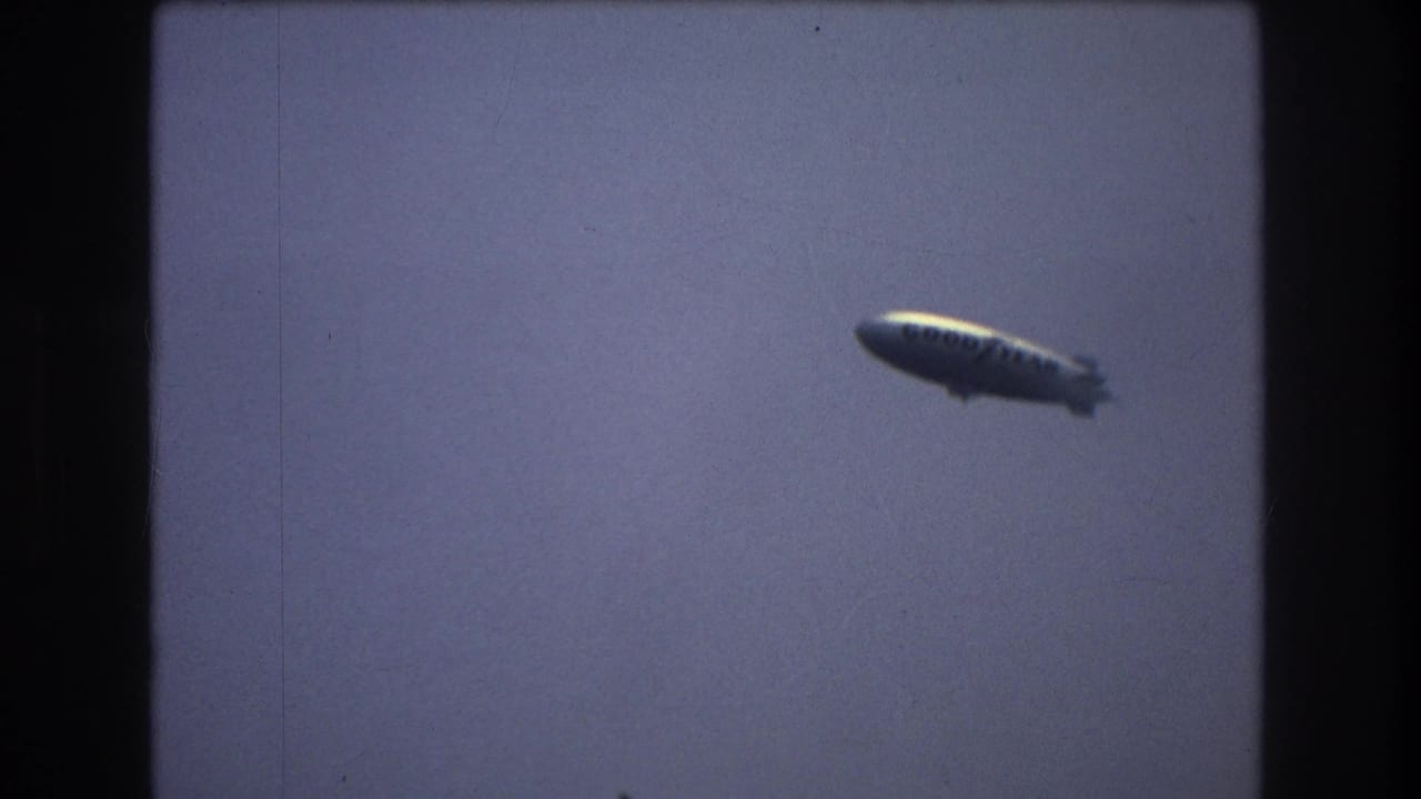 A blimp appears in a hazy sky over the New York City harbor skyline in vintage 8mm footage from the supplied 1976 metadata.