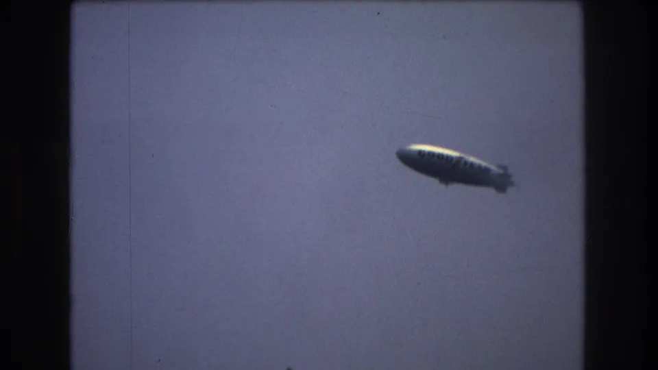A blimp appears in a hazy sky over the New York City harbor skyline in vintage 8mm footage from the supplied 1976 metadata.