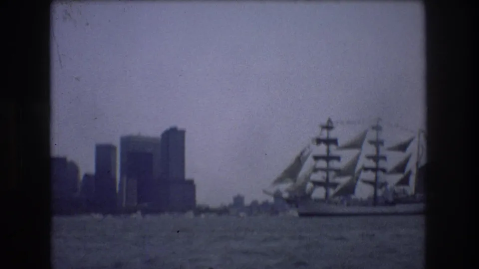 The tall ship is more fully visible on the harbor, with masts, sails, and rigging set against the hazy New York City skyline.