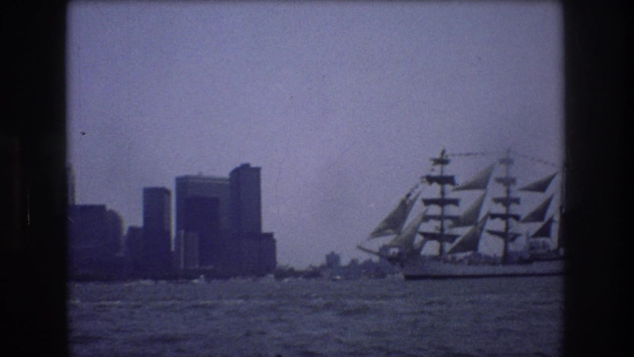 1976 New York City waterfront view with a multi-masted sailing ship moving across choppy water before a distant skyline.