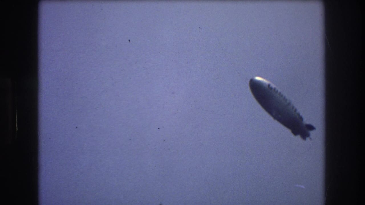 Silver blimp flying through a hazy sky.