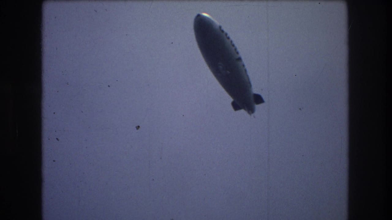 The Goodyear airship is seen at an angle in the sky, framed by dark 8mm borders and muted color consistent with the supplied 1976 New York City metadata.