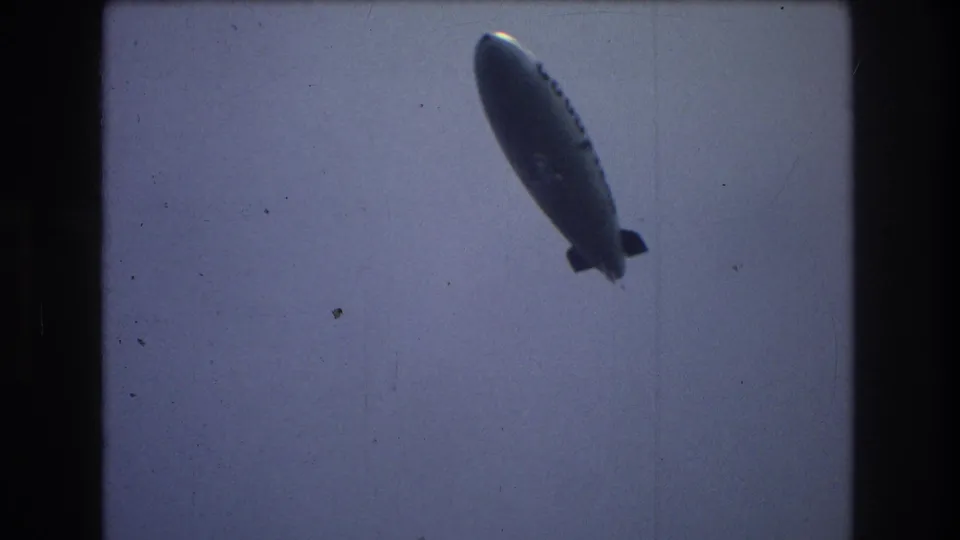 The Goodyear airship is seen at an angle in the sky, framed by dark 8mm borders and muted color consistent with the supplied 1976 New York City metadata.