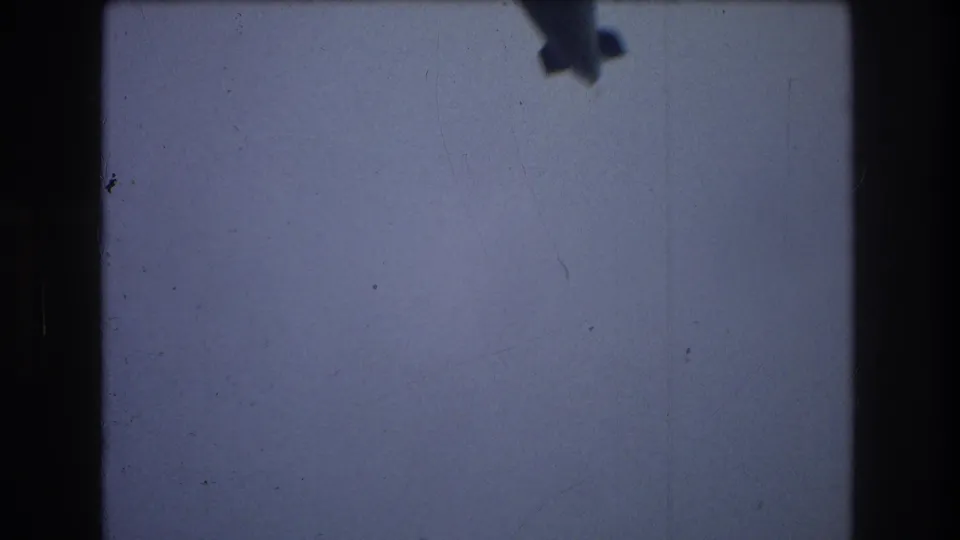 A partial, motion-blurred view of the airship passes near the lower part of the frame, leaving mostly pale sky and visible 8mm film texture.