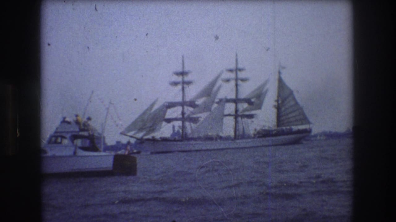 1976 New York City home-movie frame showing a multi-masted sailing ship with sails raised passing behind a small motorboat on harbor water.