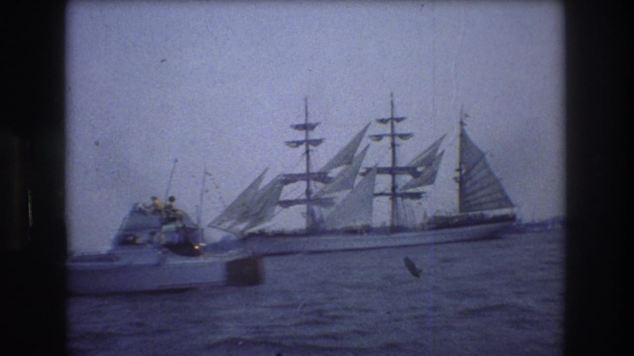 Small motorboat in the foreground with a large sailing ship moving across the water behind it.