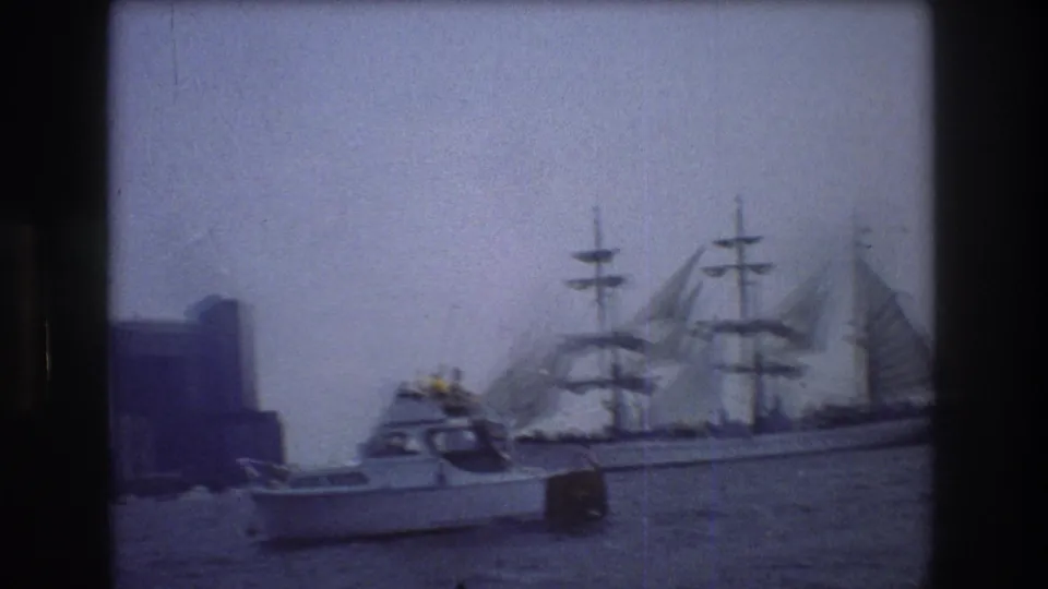 Late frame from the 1976 New York City home movie showing the sailing ship moving near the edge of the frame while a small motorboat remains in the foreground.
