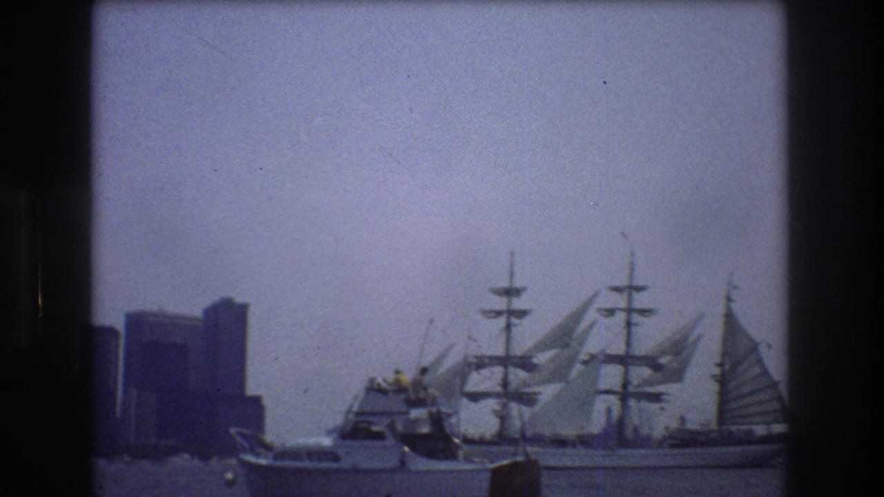 Small motorboat crosses in front of a three-masted sailing ship near a city skyline.