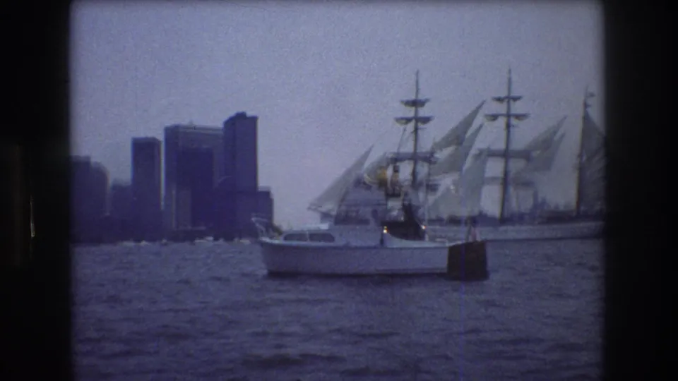 The motorboat is centered in the frame with the three-masted sailing ship and New York City skyline receding behind it across the harbor.
