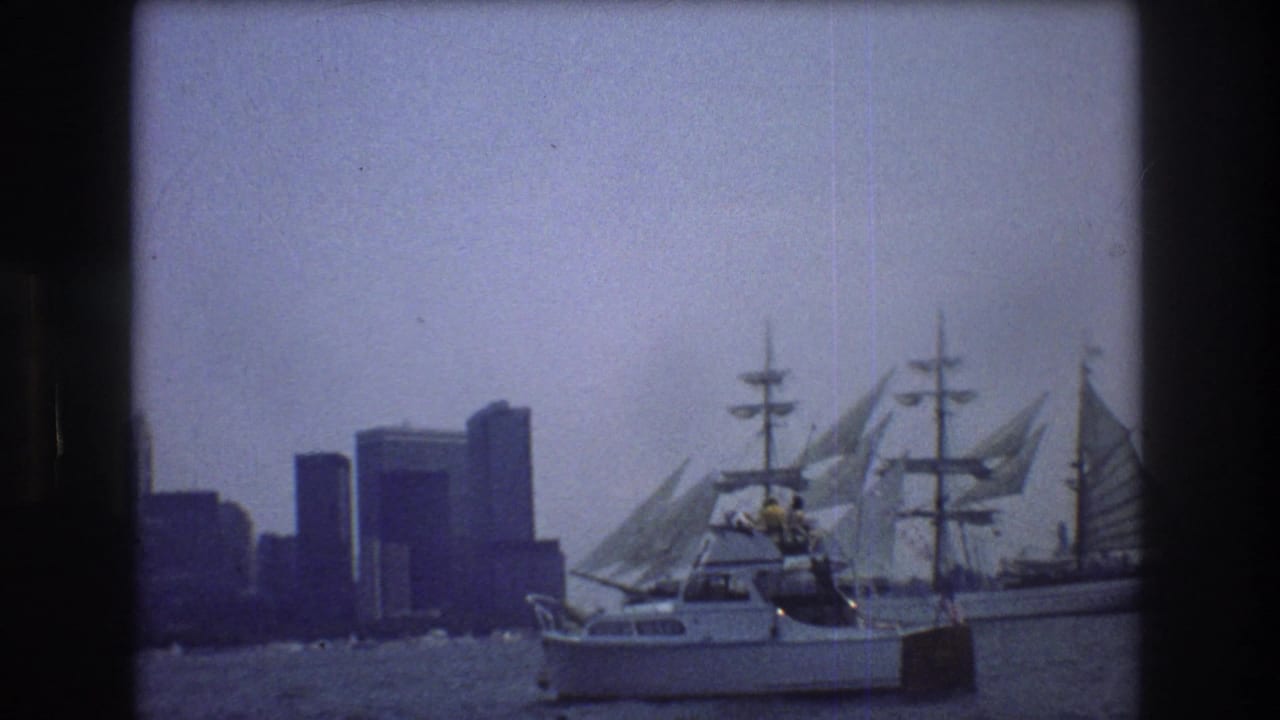 Motorboat and sailing ship on harbor water with dark city buildings in the background.