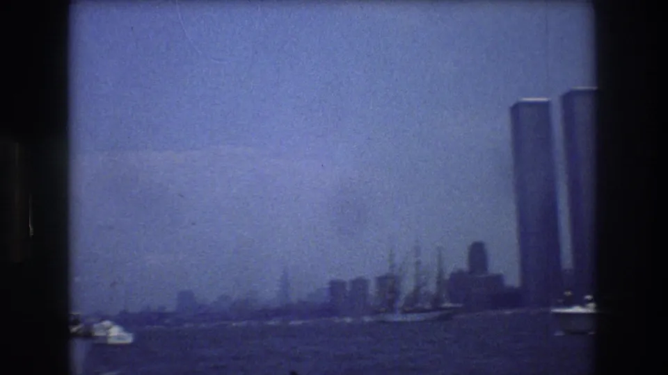 1976 8mm view across New York Harbor toward the Manhattan skyline, with the Twin Towers prominent at the right and small boats on the water.