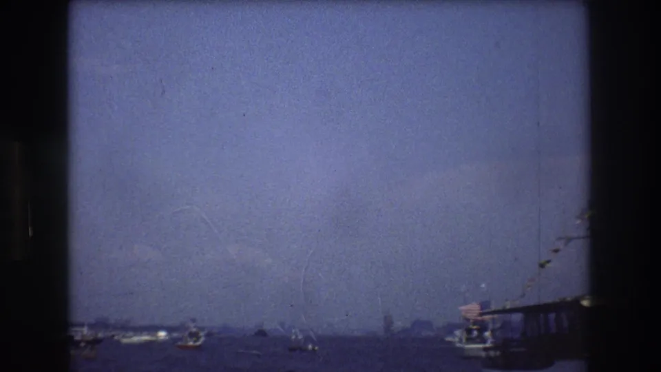 1976 New York City harbor footage showing small boats on open water, a hazy skyline, and the edge of a larger structure or vessel at the right side of frame.
