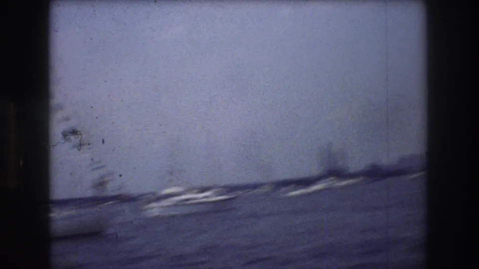 Handheld 8mm view across New York City harbor, with blurred boats, open water, and a faint urban shoreline under a pale sky.