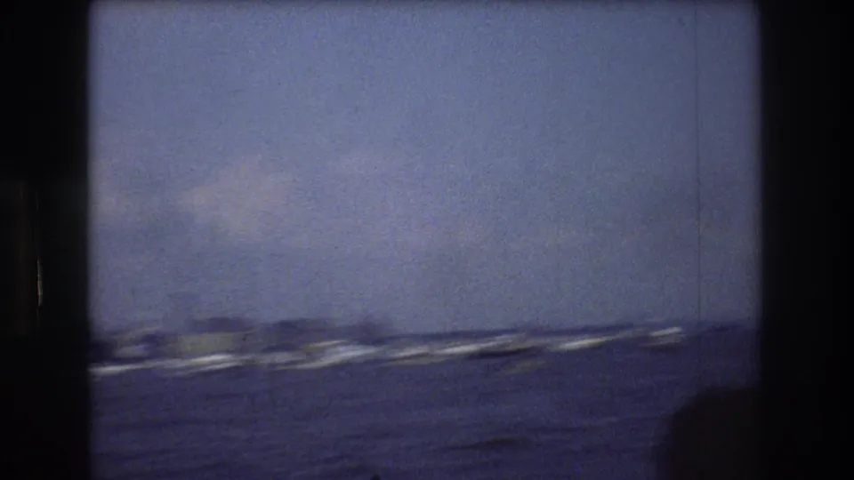 Open water in New York Harbor, with small boats and a faint distant shoreline seen through the soft, grainy 8mm frame.
