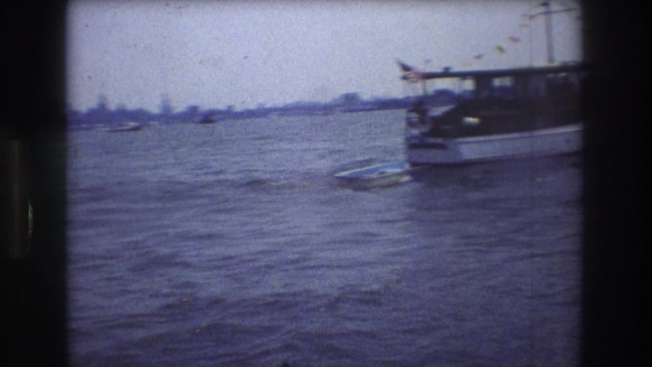 1976 New York City 8mm frame showing a white motorboat partly cropped at right, rippled harbor water, and a hazy distant shoreline.
