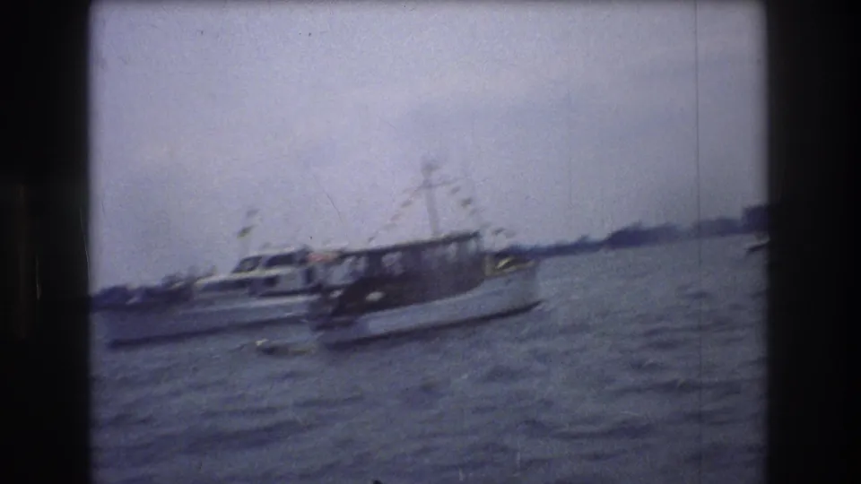 1976 New York City 8mm frame with a blurred white motorboat and another nearby vessel on open water, seen through soft handheld film motion.