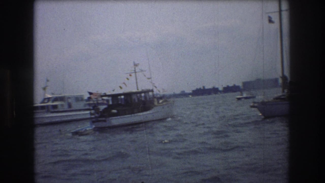 1976 New York City harbor footage showing a white motorboat with an American flag and bunting moving across choppy water near other boats.