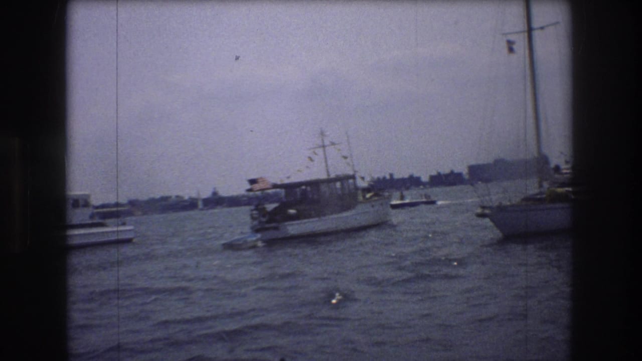 Decorated motorboat passing across harbor water with sailboat masts at the edge of frame.