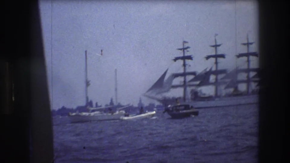 A large multi-masted sailing ship appears on the right side of the New York City harbor view, with smaller boats and rough water in the foreground.