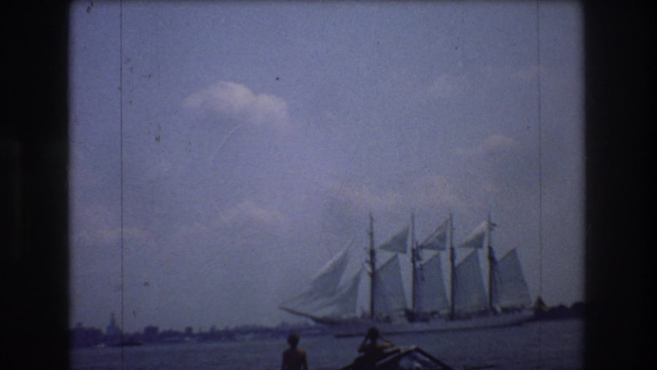 1976 8mm New York City harbor frame showing a multi-masted sailing ship under sail while two boating onlookers watch from the foreground.