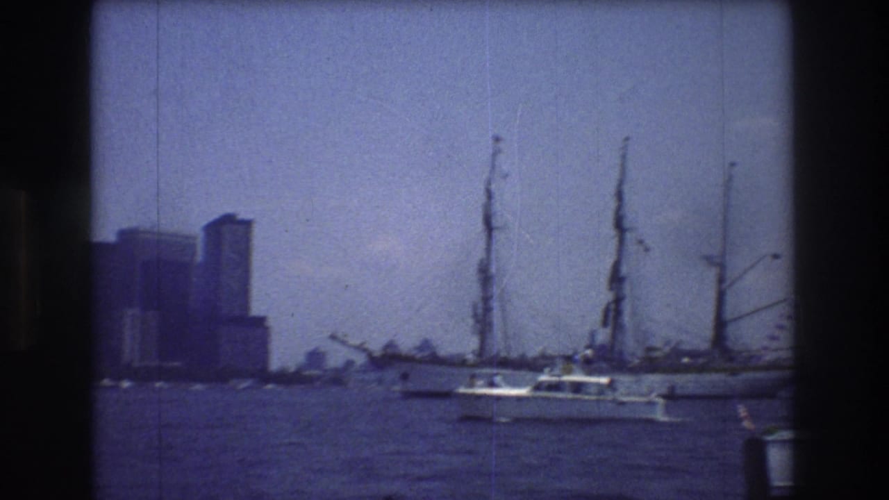 1976 8mm home-movie frame showing a large sailing vessel with furled sails and a small motorboat on New York City harbor before a hazy Manhattan skyline.