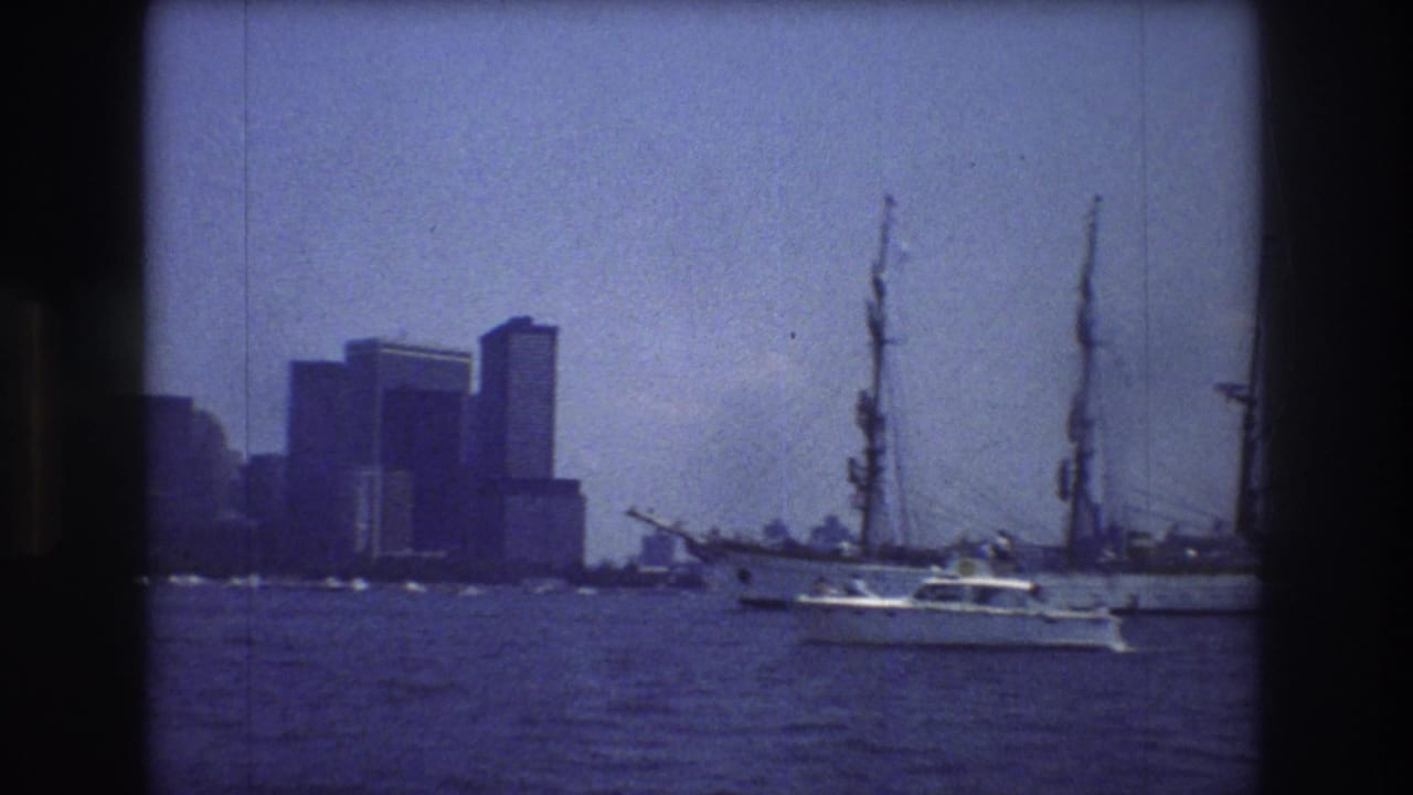 Small motorboat moves near a large sailing vessel on harbor water with high-rise buildings behind.
