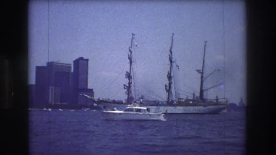 The final 8mm frame shows a tall-masted sailing ship on New York City harbor with a small motorboat crossing in front and Manhattan buildings beyond.