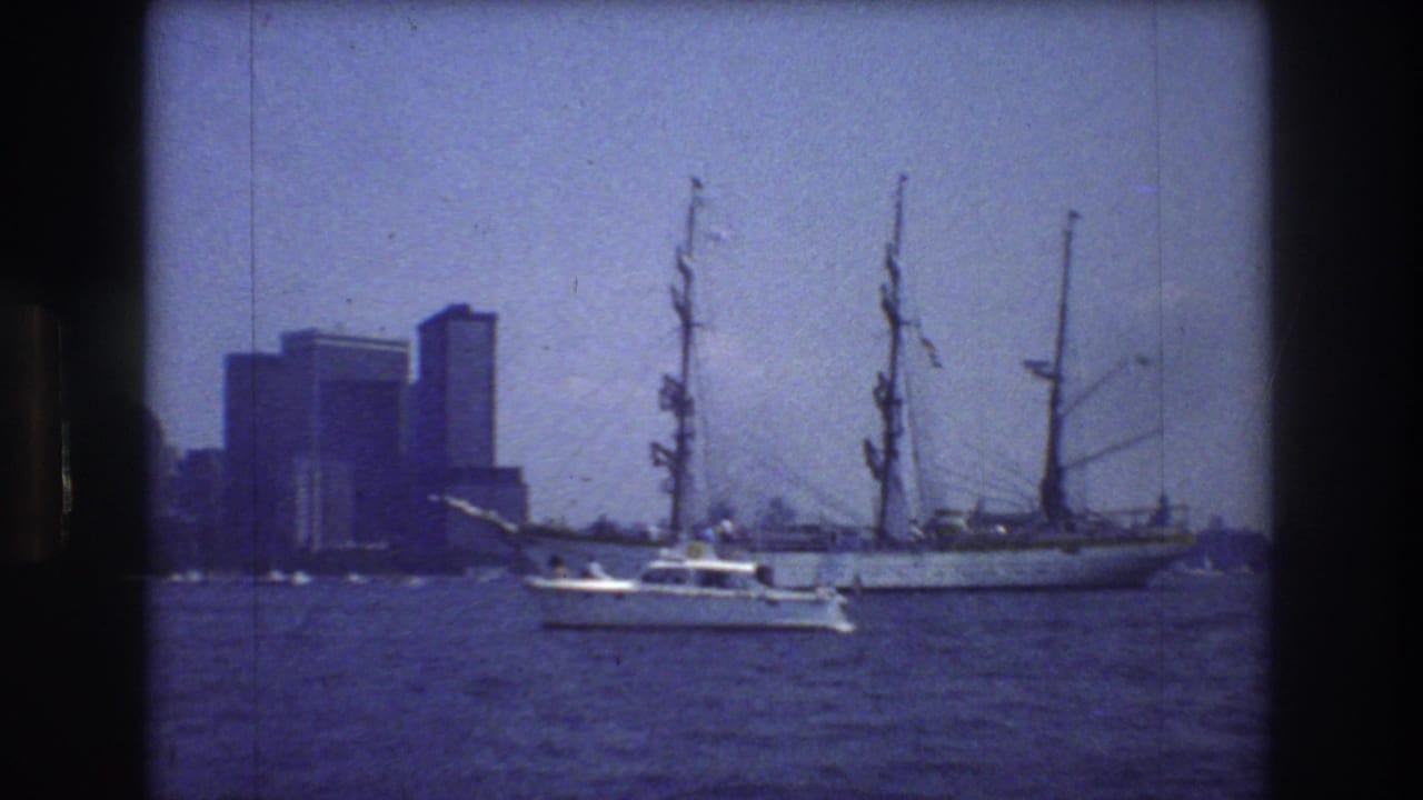 1976 New York City harbor view showing a large white multi-masted sailing ship, a small motorboat crossing the foreground, and distant high-rise buildings under a blue cast.