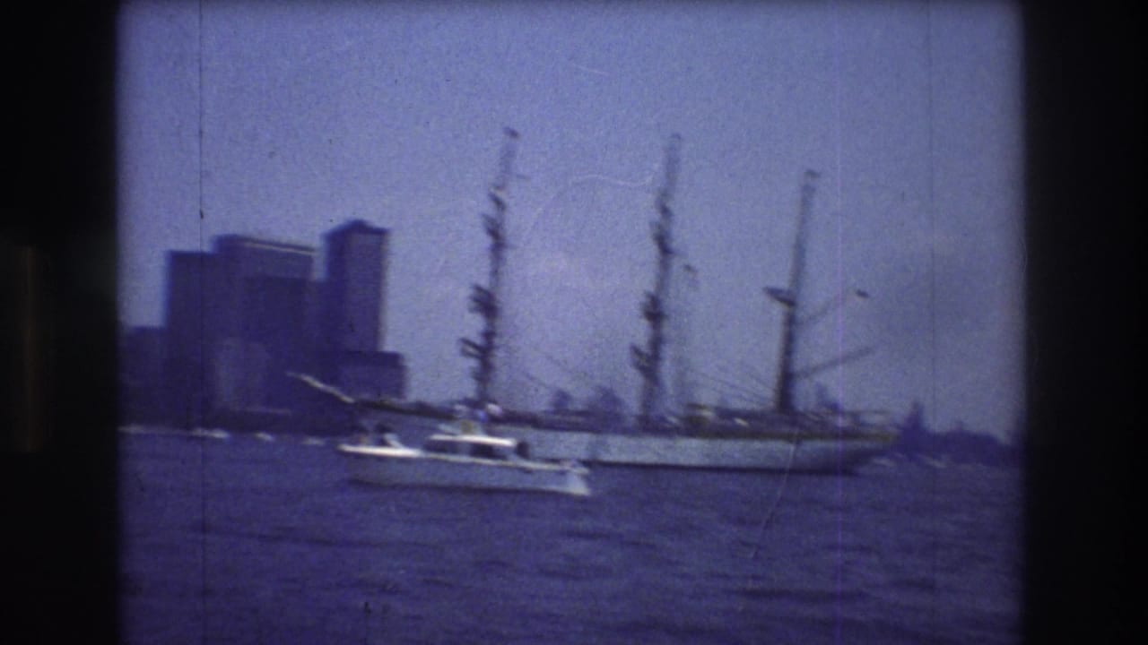 1976 New York City harbor frame with a small white motorboat moving across the water before a large multi-masted sailing ship and distant skyline.